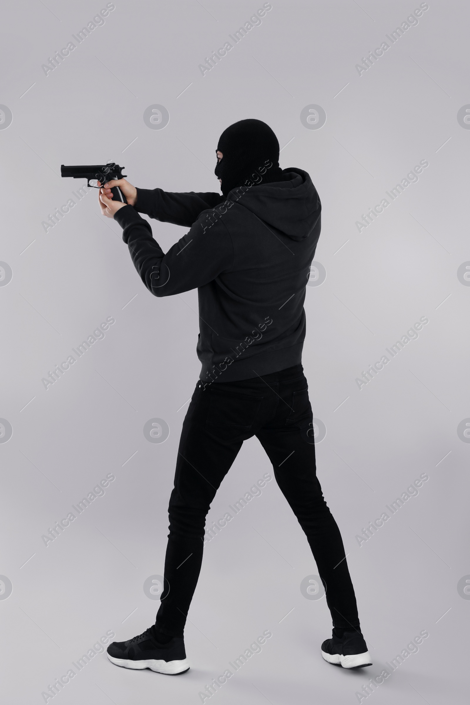 Photo of Man wearing black balaclava with gun on light grey background