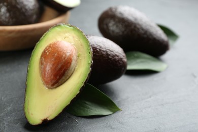 Whole and cut avocados with green leaves on grey table, closeup