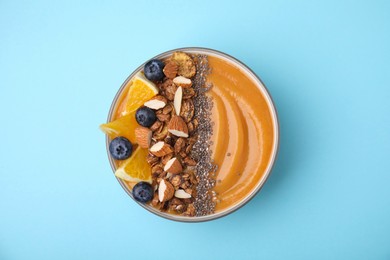 Photo of Bowl of delicious fruit smoothie with fresh orange slices, blueberries and granola on light blue background, top view
