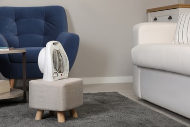 Photo of Electric fan heater on pouf in living room