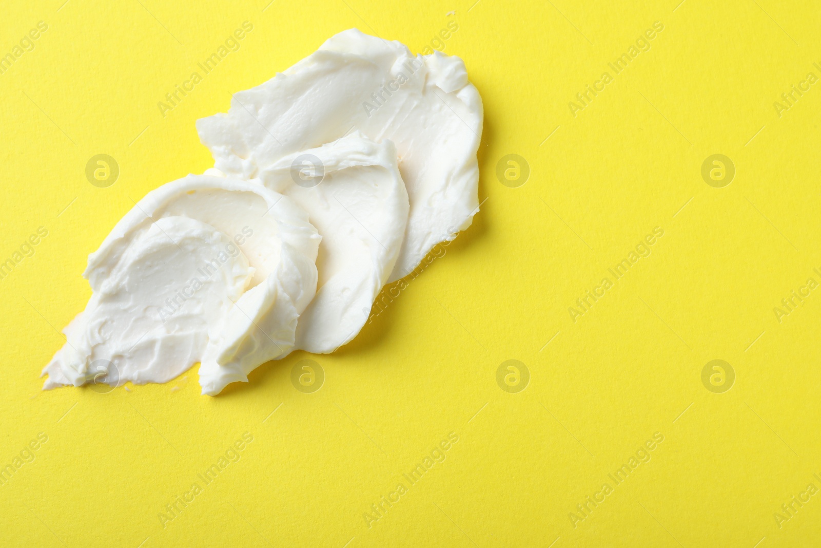 Photo of Smear of delicious cream cheese on yellow background, top view. Space for text