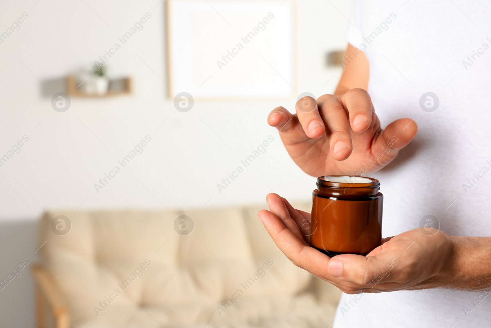 Photo of Man holding jar of hand cream at home, closeup. Space for text