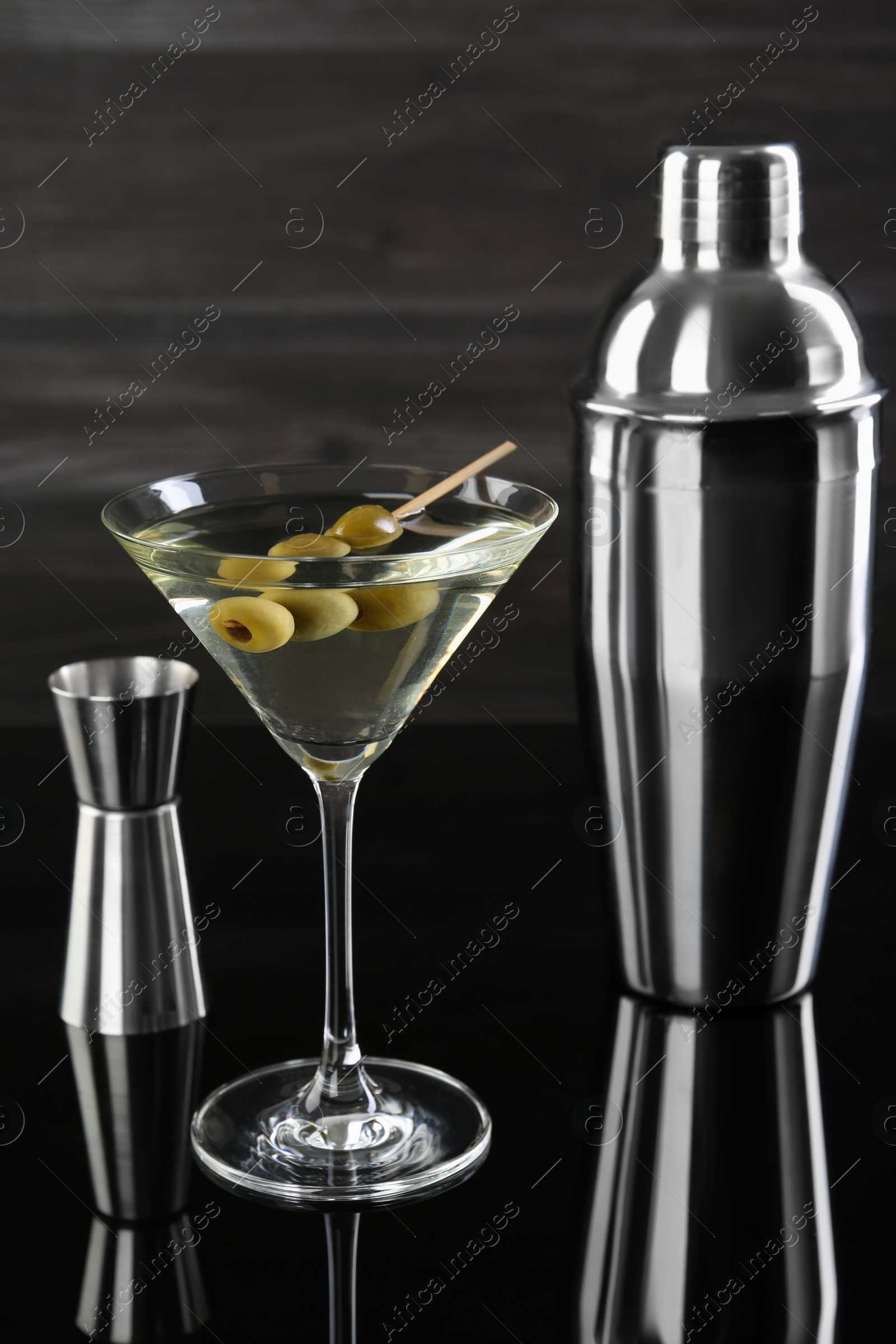 Photo of Metal shaker, Martini cocktail and jigger on black mirror surface