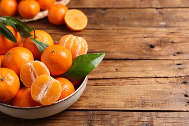 Fresh tangerines with green leaves in bowl on wooden table, space for text