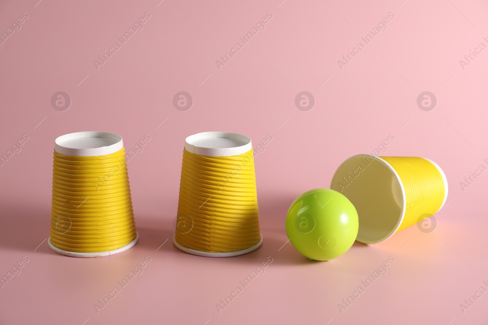 Photo of Shell game. Three yellow cups and ball on pink background