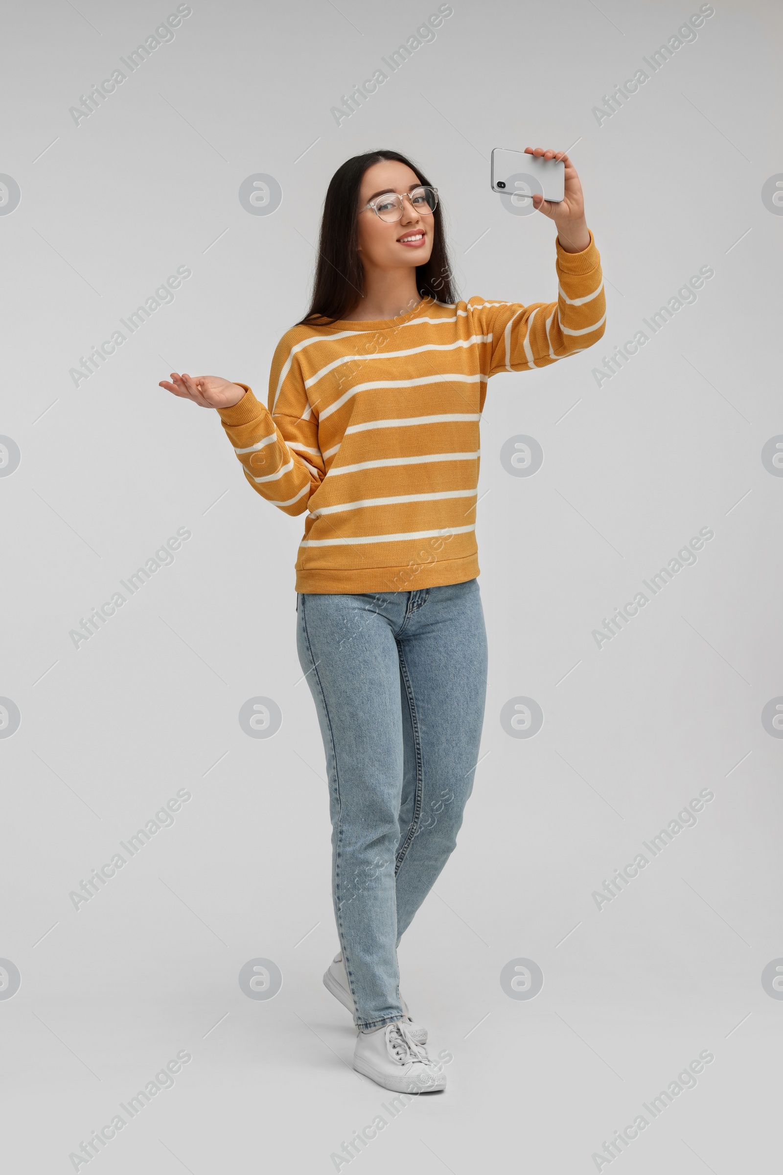 Photo of Smiling young woman taking selfie with smartphone on white background