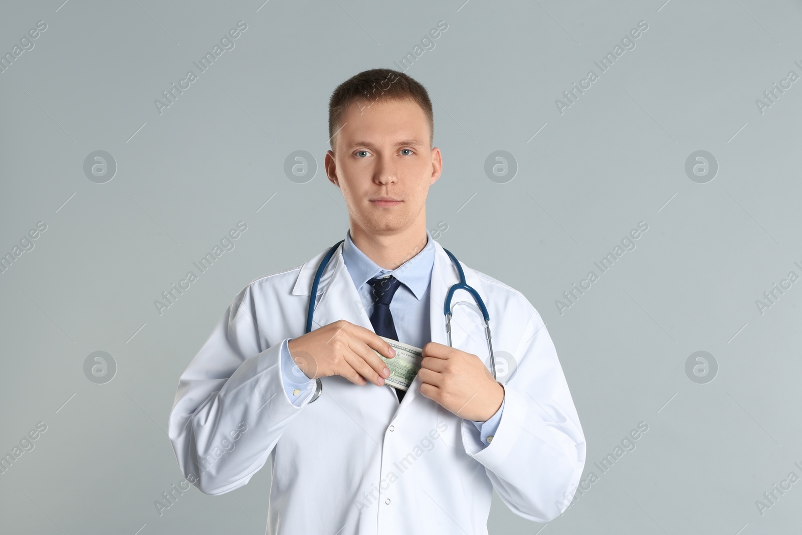Photo of Doctor putting bribe into pocket on grey background. Corruption in medicine