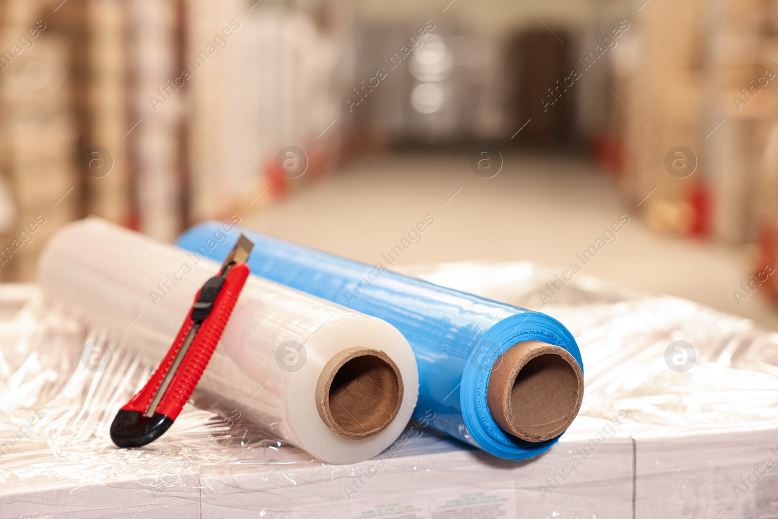 Photo of Rolls of different stretch wraps and utility knife on boxes in warehouse