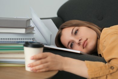 Photo of Young tired woman with coffee lying on couch indoors