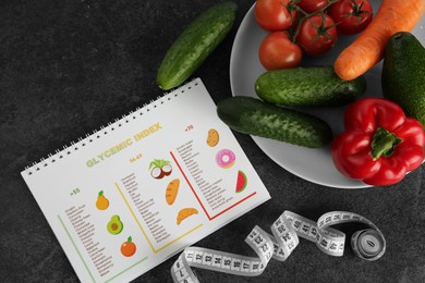 Photo of Notebook with information about glycemic index, measuring tape and vegetables on grey table, flat lay