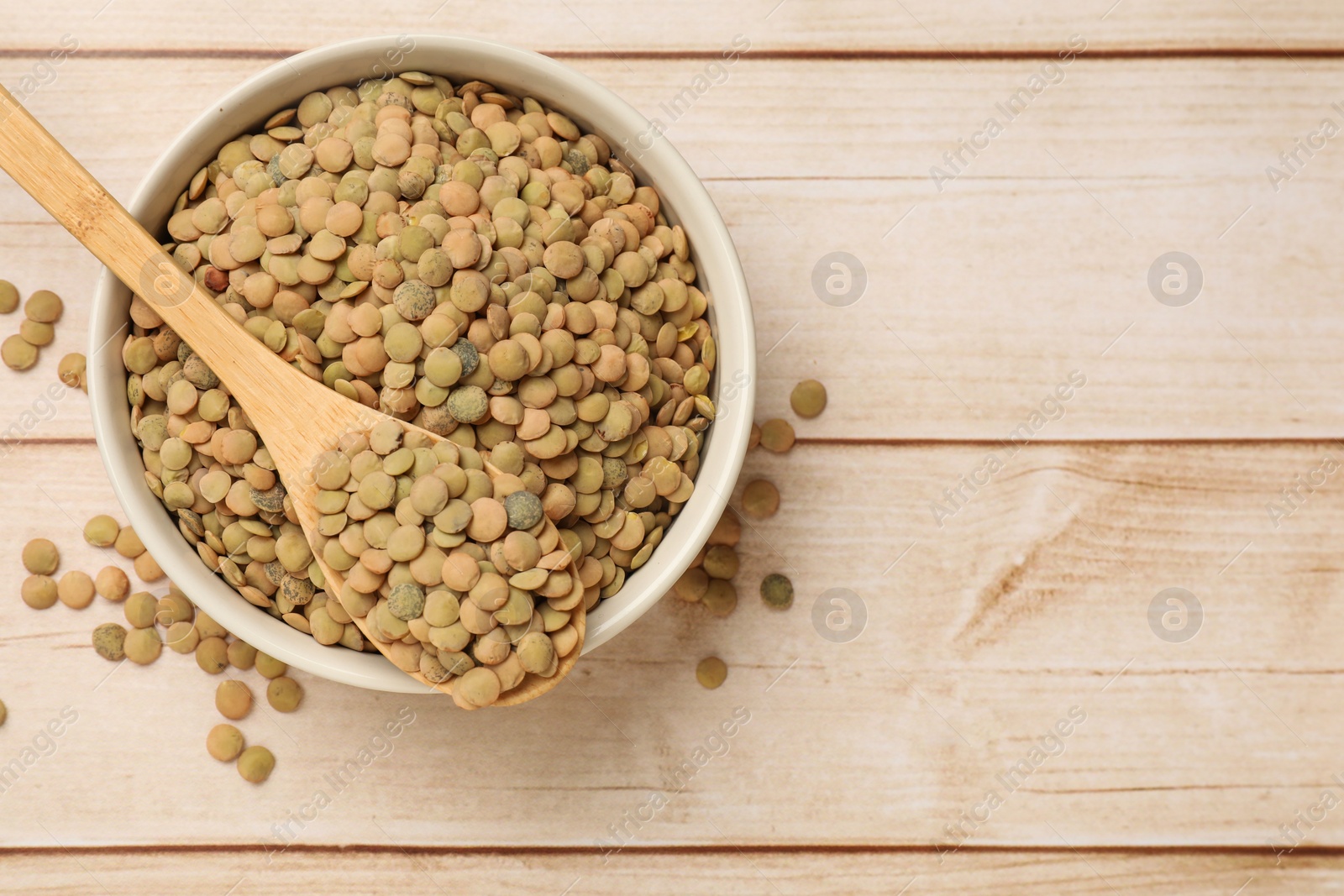 Photo of Raw lentils in bowl and spoon on light wooden table, top view. Space for text