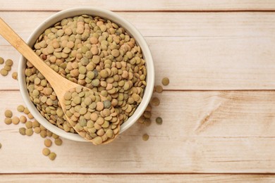 Photo of Raw lentils in bowl and spoon on light wooden table, top view. Space for text