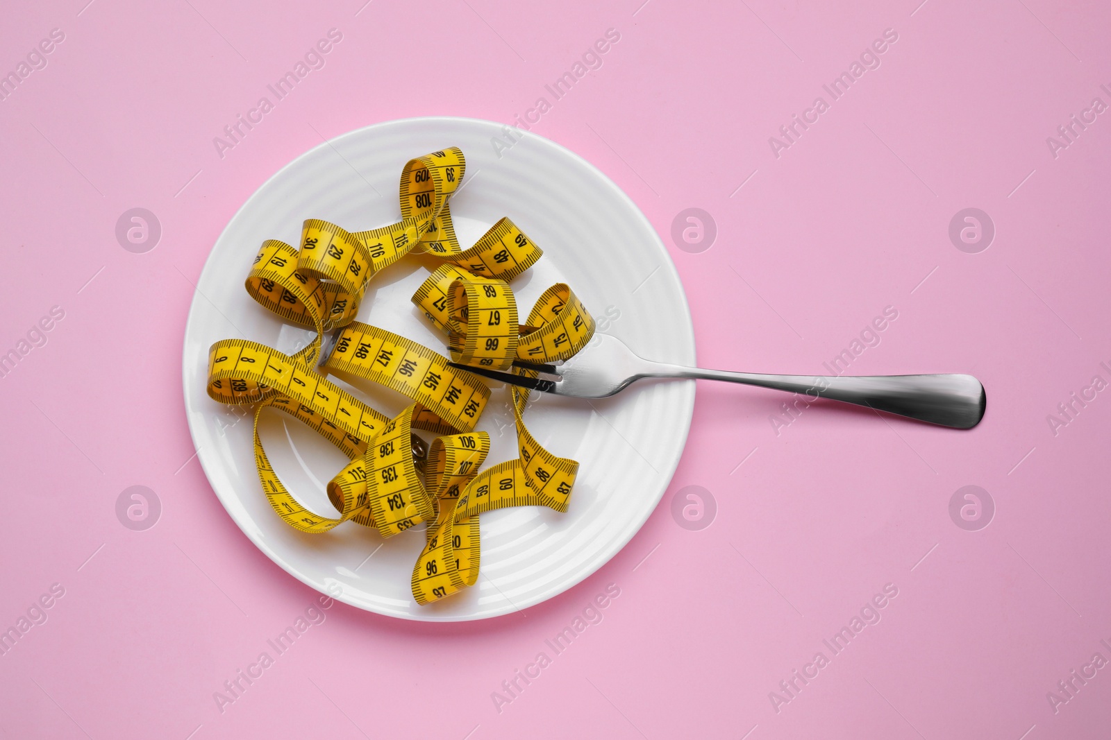 Photo of Measuring tape and fork on pink background, top view. Weight loss concept