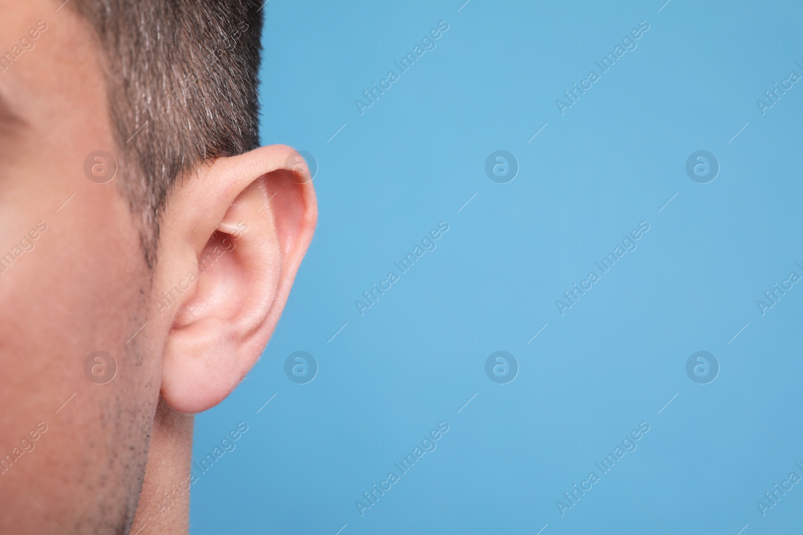 Photo of Man on light blue background, closeup of ear. Space for text