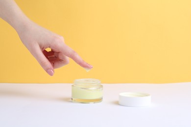 Woman with jar of cream on yellow background, closeup