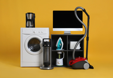 Photo of Set of different home appliances with vacuum cleaner on yellow background