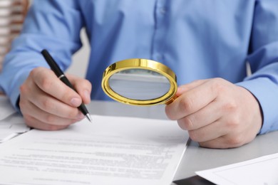 Man looking at document through magnifier at white table, closeup. Searching concept