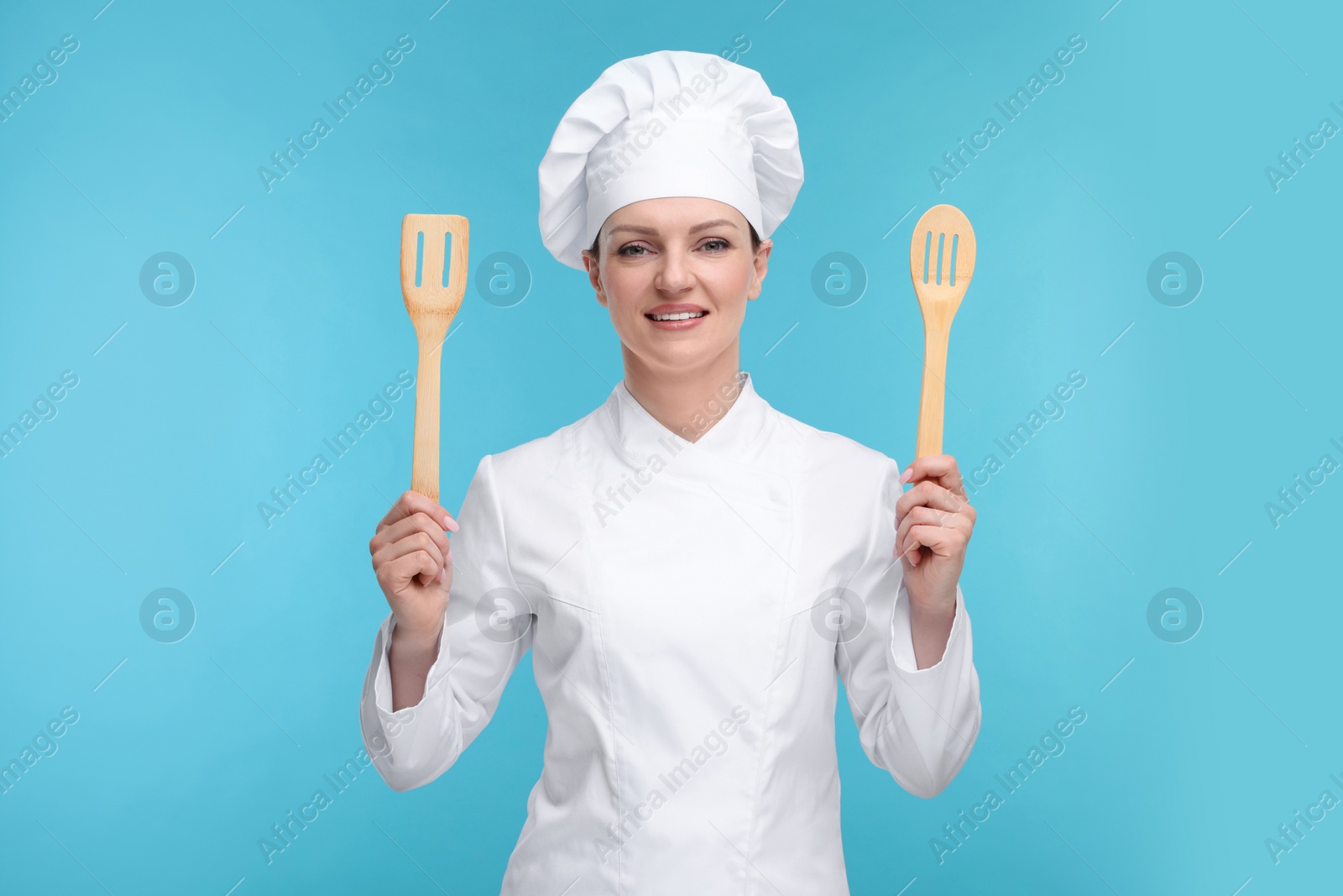 Photo of Happy chef in uniform holding wooden spatulas on light blue background