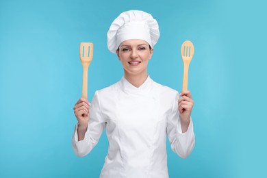 Photo of Happy chef in uniform holding wooden spatulas on light blue background