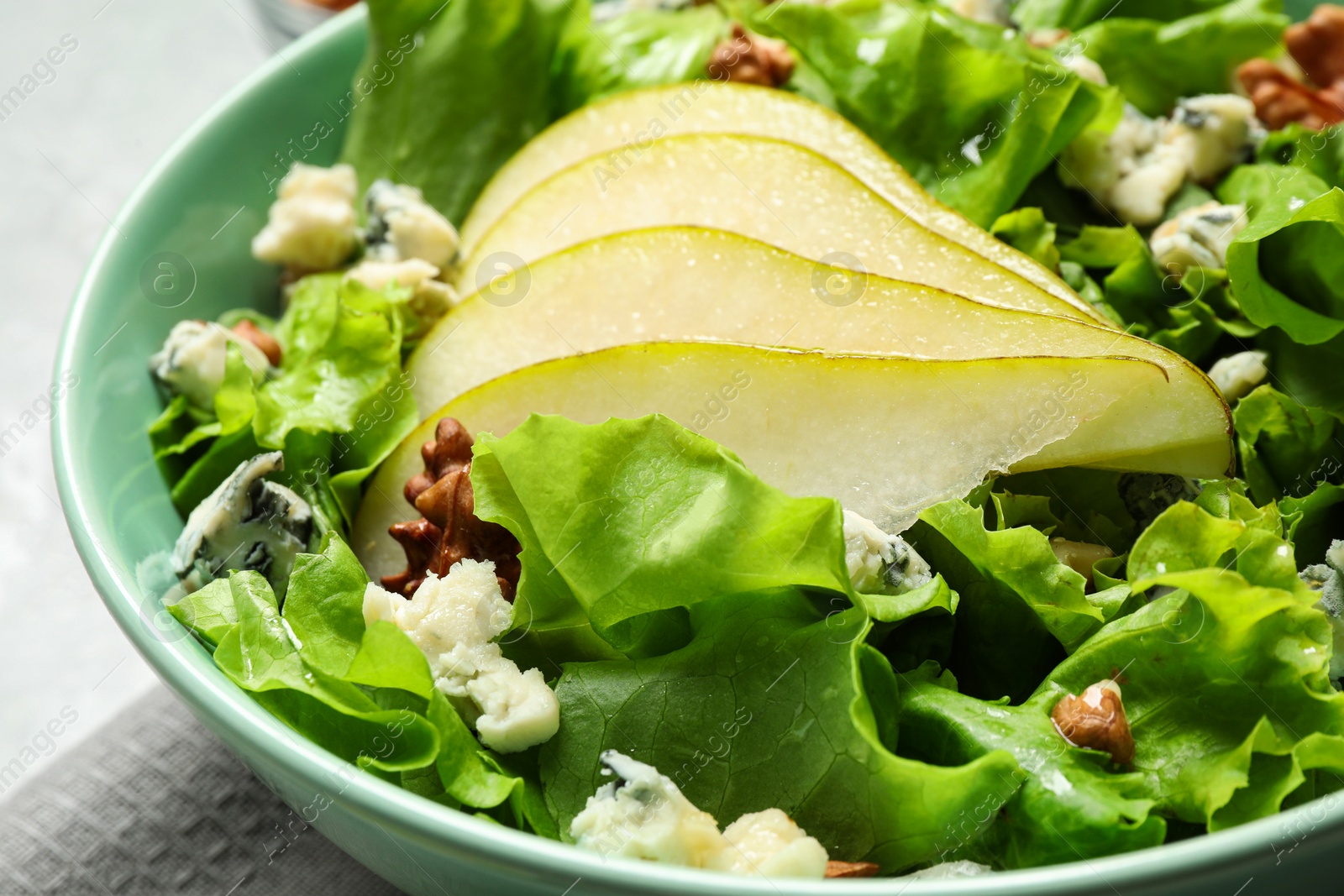 Photo of Tasty salad with pear slices, lettuce and walnuts in bowl, closeup