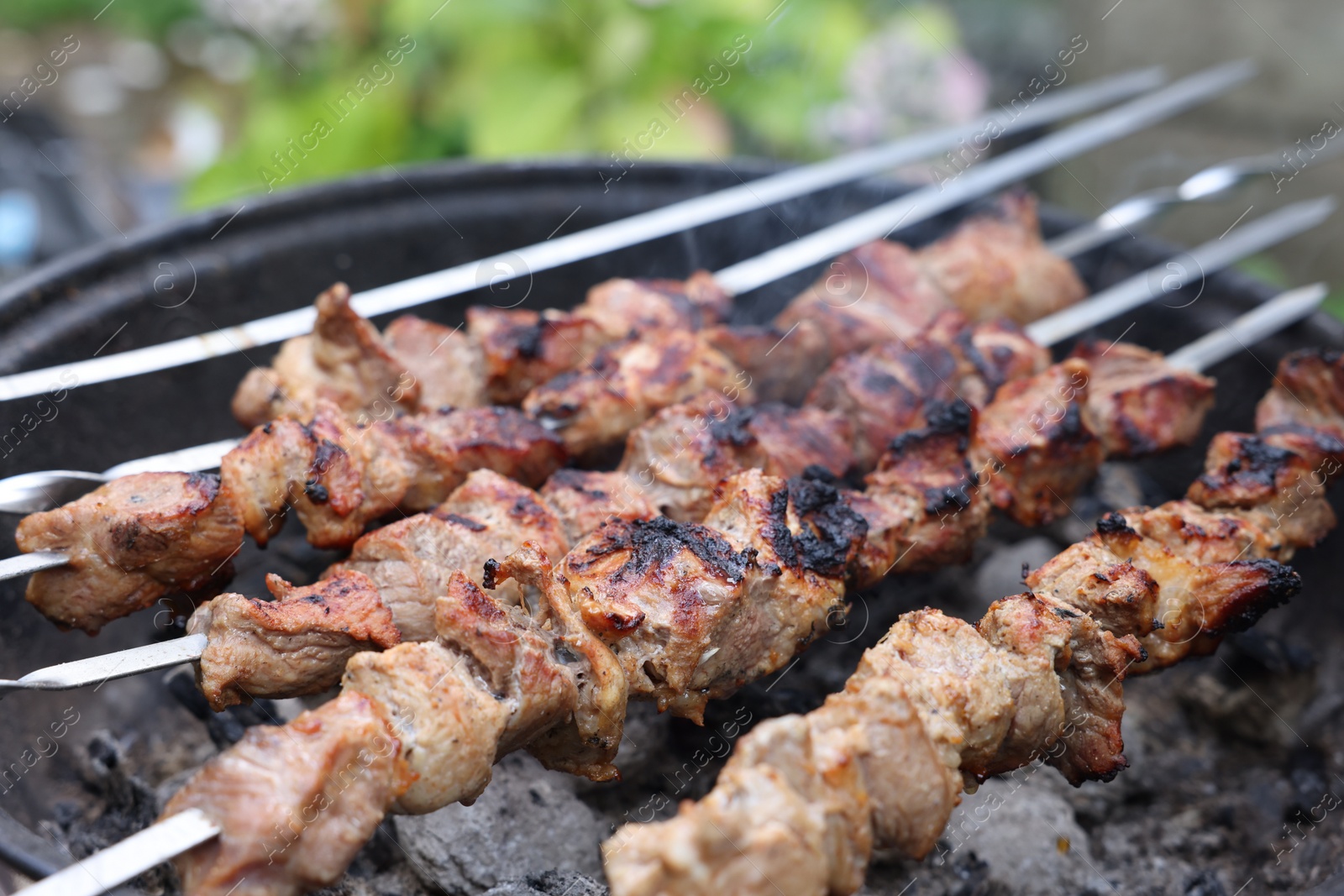 Photo of Cooking delicious kebab on metal brazier outdoors, closeup