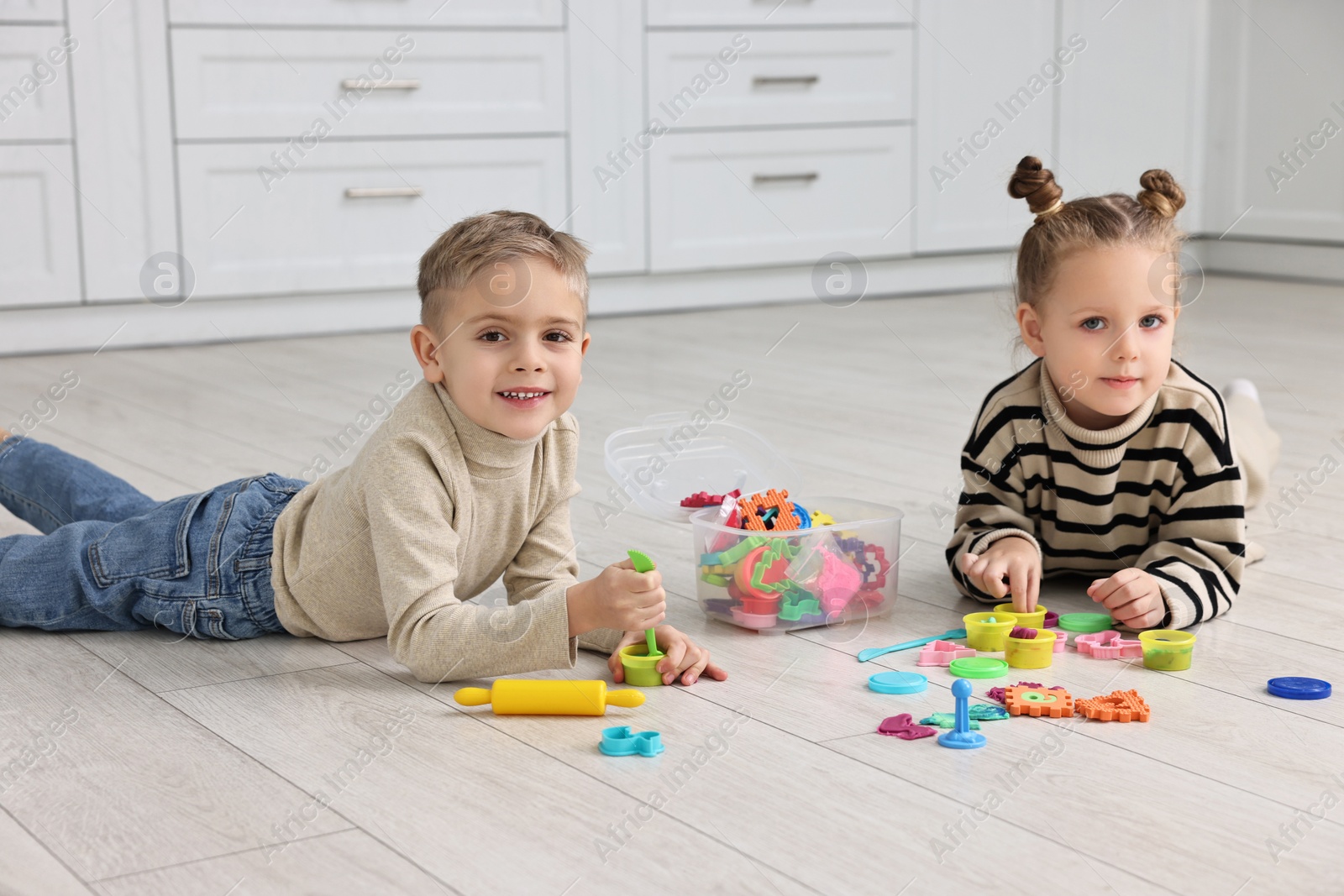 Photo of Cute little children playing together on warm floor in kitchen. Heating system