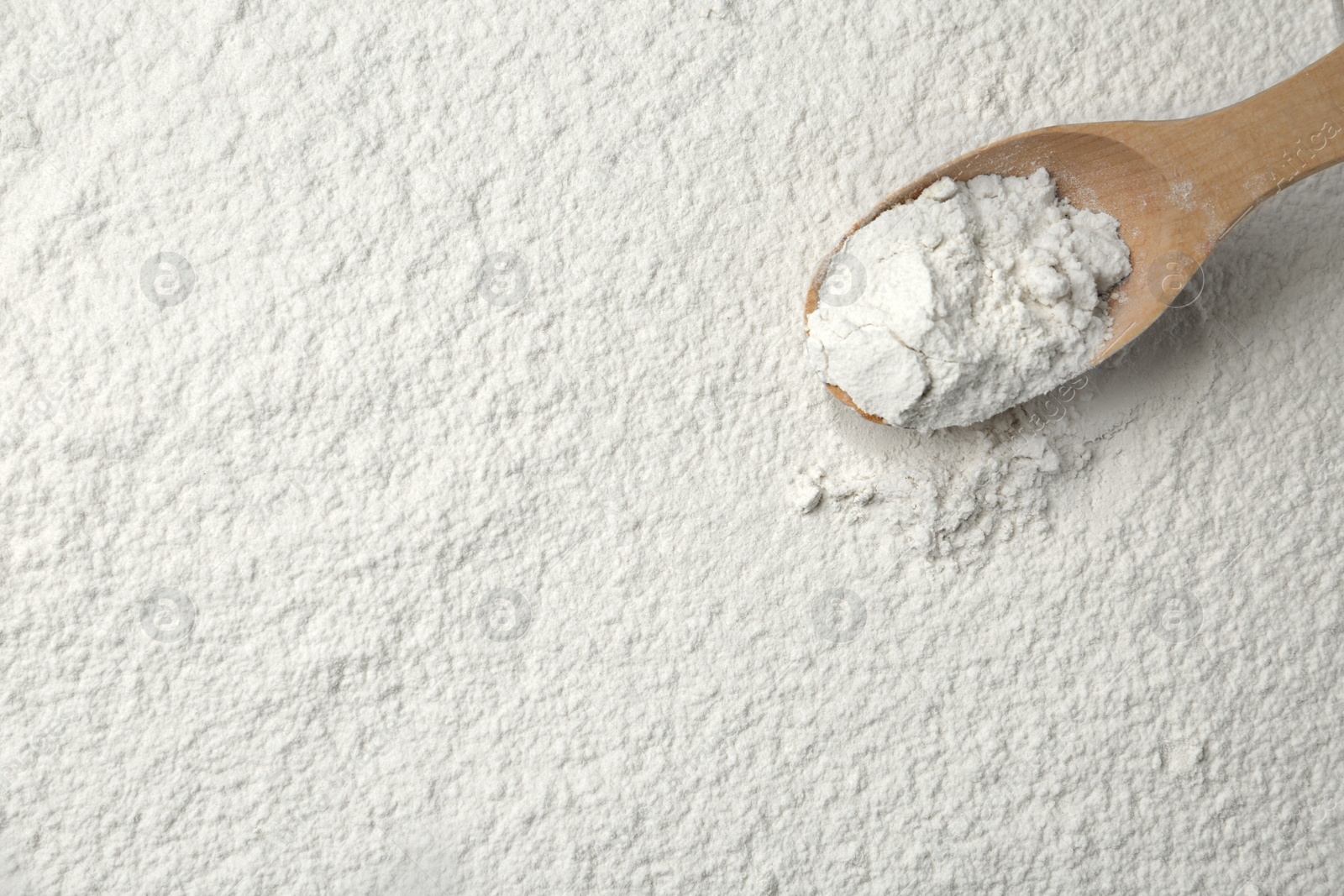 Photo of Wooden spoon on wheat flour, top view. Space for text