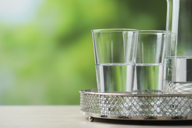 Photo of Glasses with clear water on white table against blurred green background, closeup. Space for text