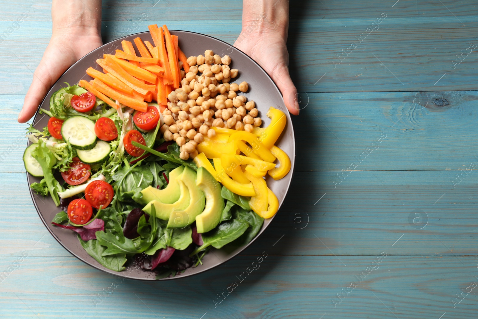 Photo of Balanced diet and vegetarian foods. Woman with plate of different delicious products at light blue wooden table, top view. Space for text