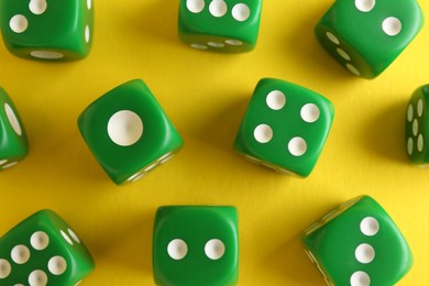 Many green game dices on yellow background, flat lay