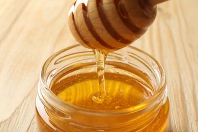 Pouring honey from dipper into jar on wooden table, closeup