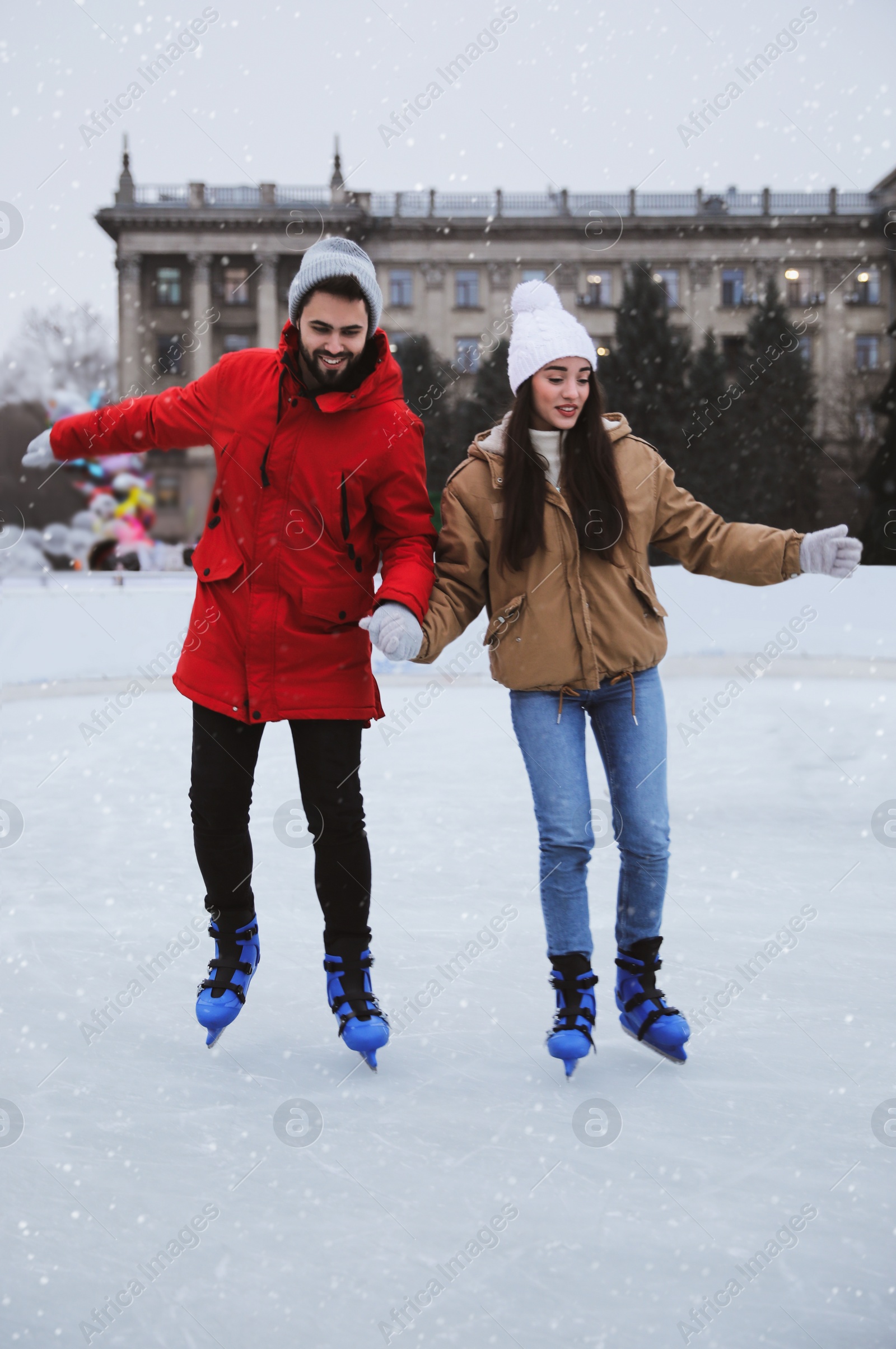 Image of Happy young couple skating at outdoor ice rink