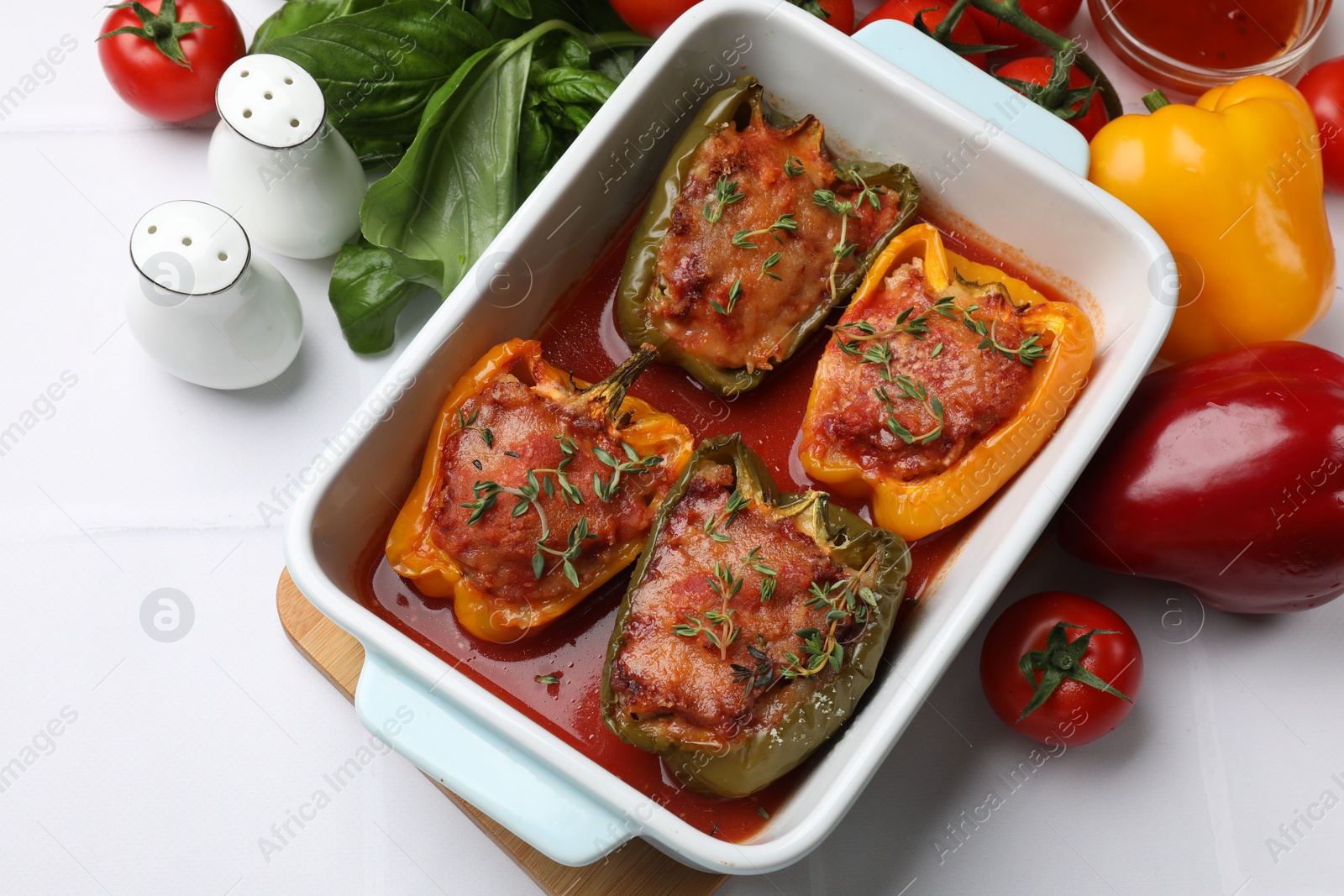 Photo of Tasty stuffed peppers in dish and ingredients on white tiled table, above view