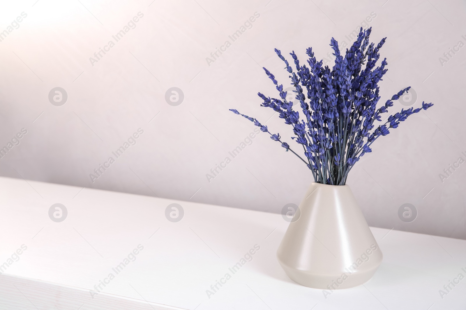 Photo of Bouquet of beautiful preserved lavender flowers on white wooden table near beige wall, closeup. Space for text