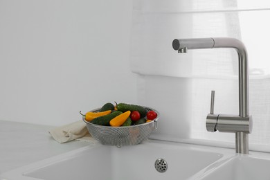 Modern sink with water tap and fresh vegetables near window in kitchen