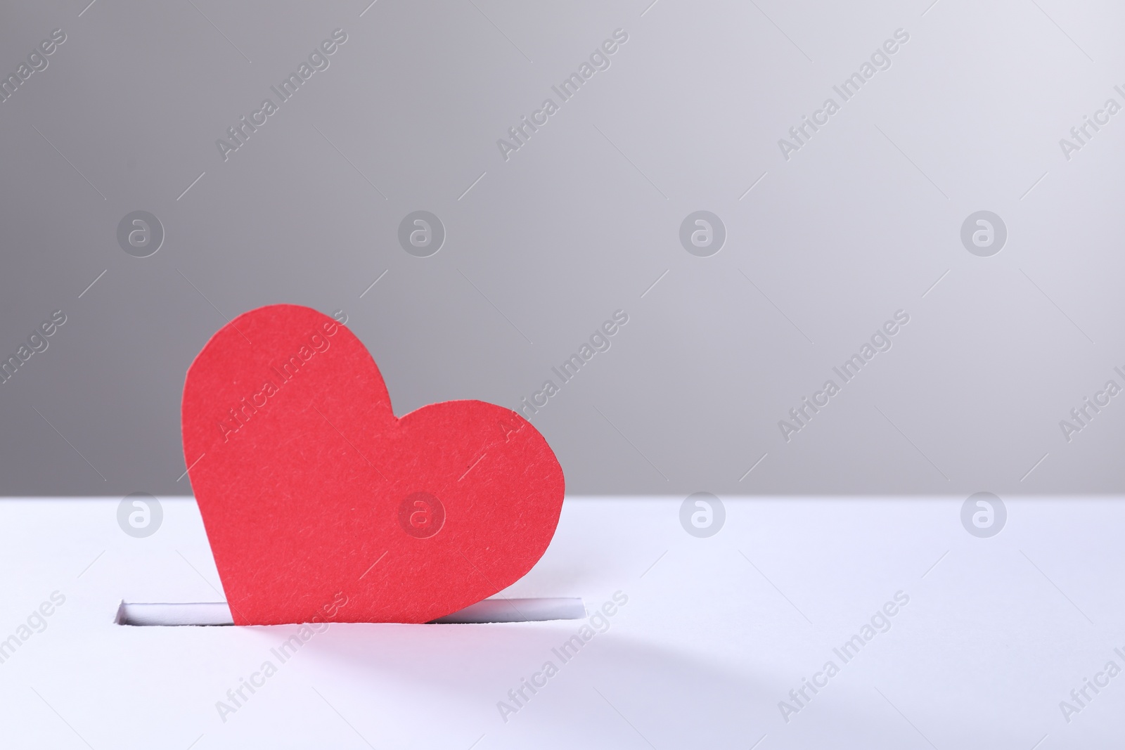 Photo of Red heart into slot of donation box against grey background, space for text