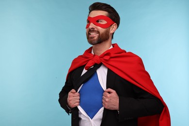 Photo of Happy businessman wearing superhero costume under suit on light blue background