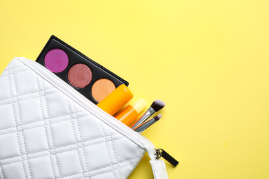 Bag with hygienic lipsticks and cosmetic products on yellow background, flat lay. Space for text