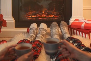 Photo of Couple with hot drinks resting near fireplace at home, closeup