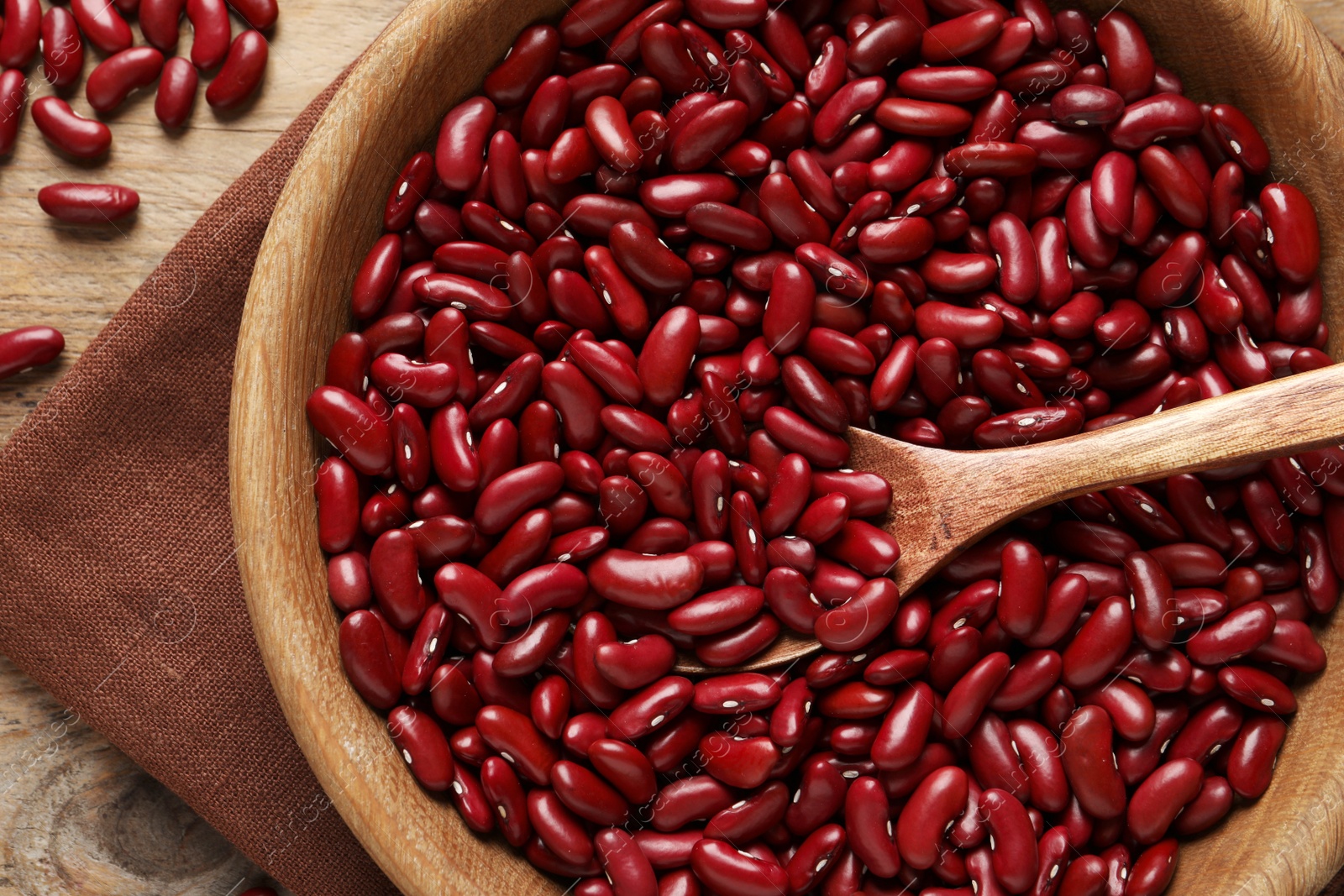 Photo of Raw red kidney beans with wooden bowl, spoon and napkin on table, top view