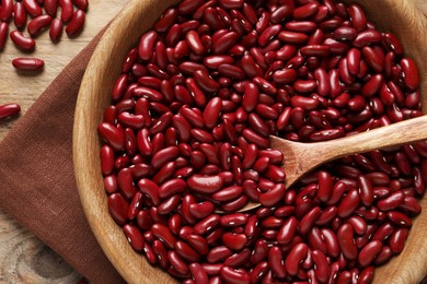 Raw red kidney beans with wooden bowl, spoon and napkin on table, top view