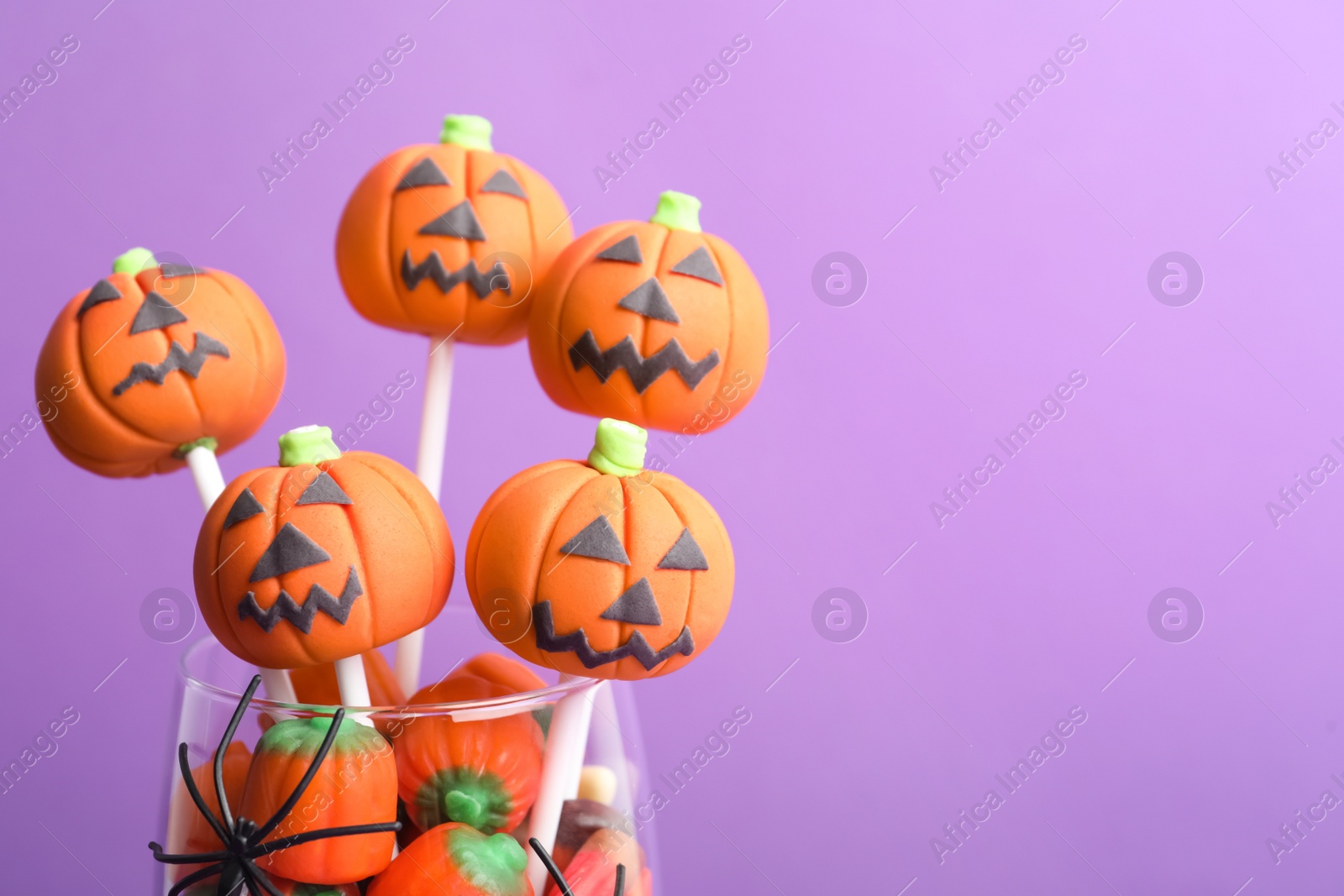 Photo of Delicious Halloween themed cake pops on violet background, closeup. Space for text