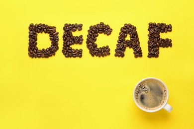 Word Decaf made with coffee beans and cup of hot drink on yellow background, flat lay. Space for text