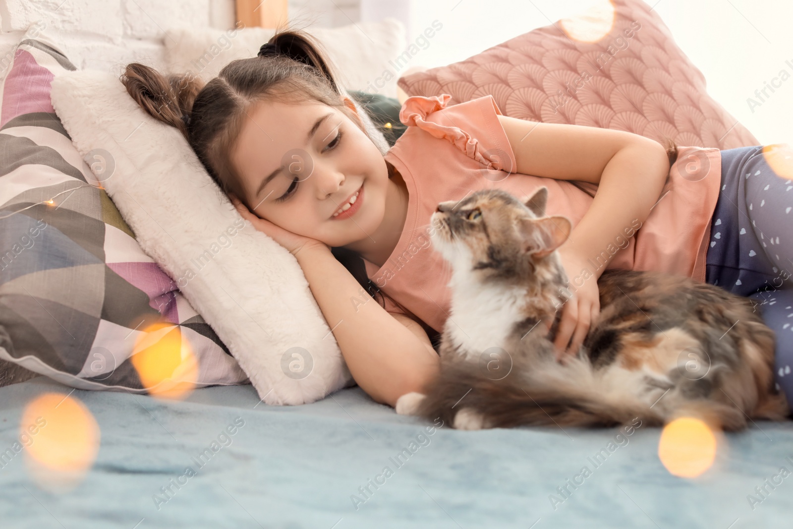 Photo of Cute little girl with cat lying on bed at home