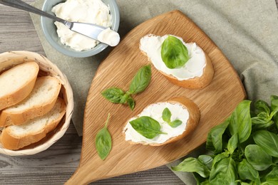 Photo of Delicious sandwiches with cream cheese and basil leaves on wooden table, flat lay