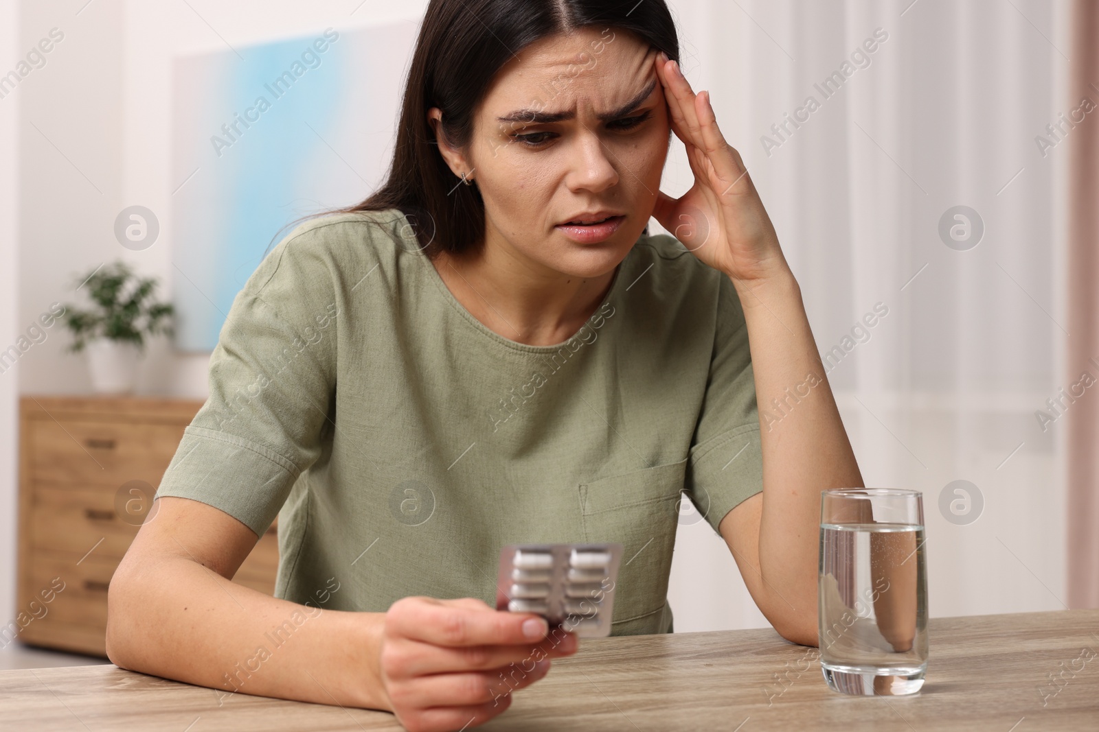 Photo of Sad woman with blister of pills suffering from headache at wooden table indoors
