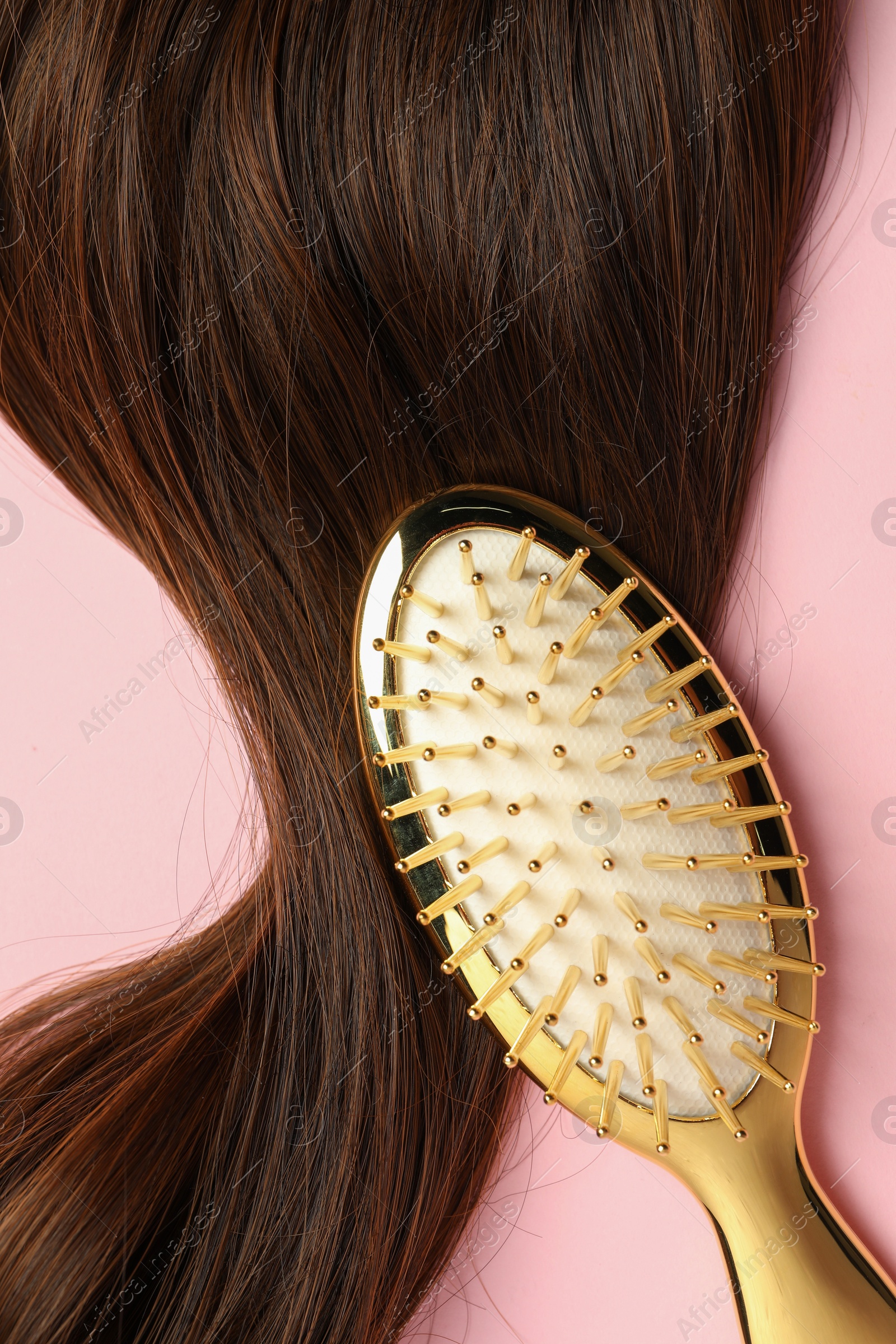 Photo of Stylish brush with brown hair strand on pink background, top view