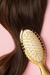 Stylish brush with brown hair strand on pink background, top view