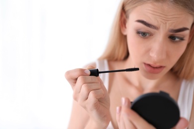 Photo of Emotional woman holding mascara brush with fallen eyelashes indoors