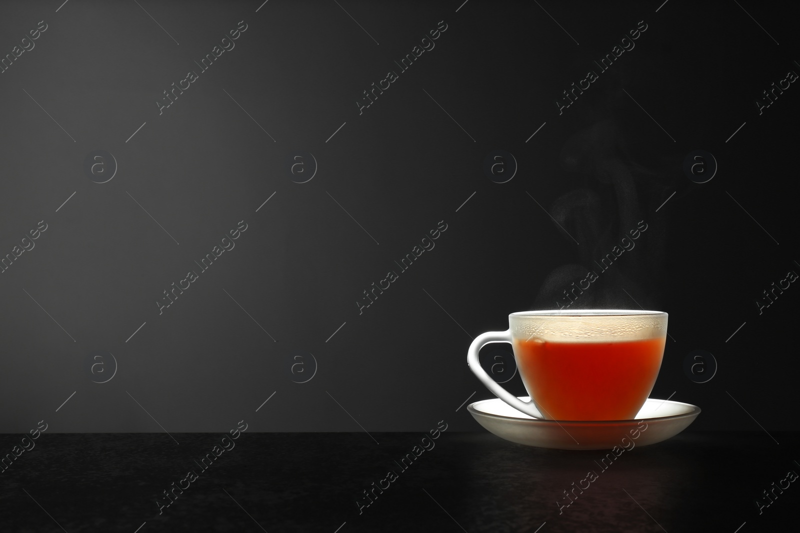 Photo of Glass cup of hot tea on stone table against grey background, space for text